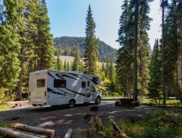 Beautiful campsite in the mountains with an RV and wooden bench.